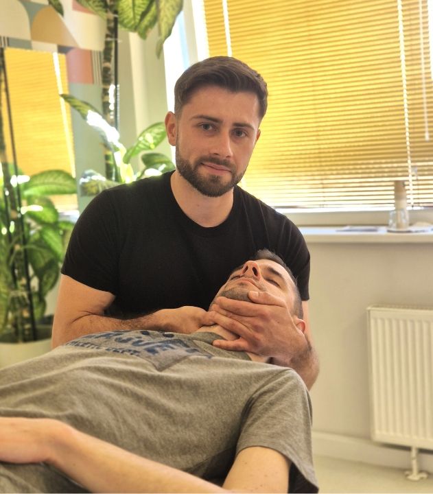Fizjoterapeuta wykonujący terapię powięziową u Pacjenta z problemami napięcia okolic szyi i karku.